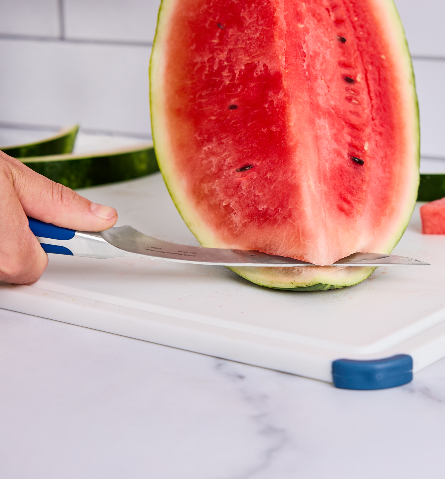 Cutting watermelon rind off with a chef's knife on a white cutting board
